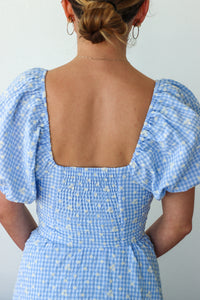 Person wearing a blue checkered dress with floral pattern on a plain background