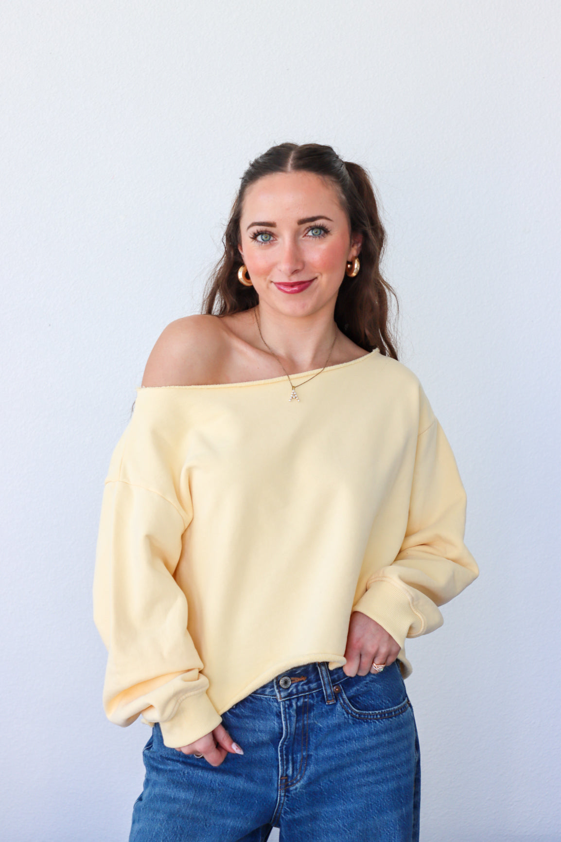 Woman wearing a yellow off-shoulder sweater and blue jeans against a white background