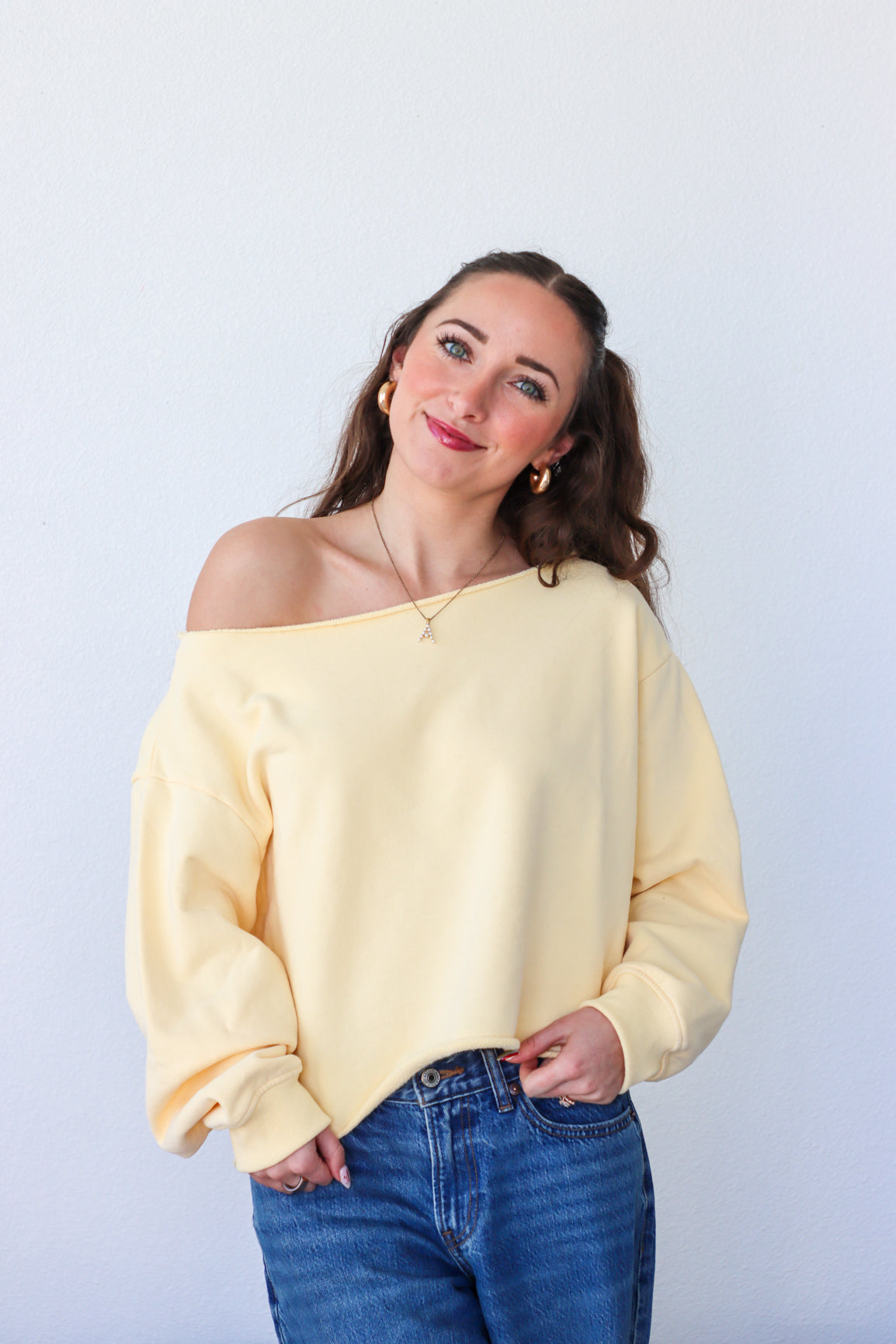 Woman wearing a yellow off-shoulder sweater and blue jeans against a white background