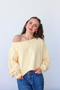 Woman wearing a yellow off-shoulder sweater and blue jeans against a white background