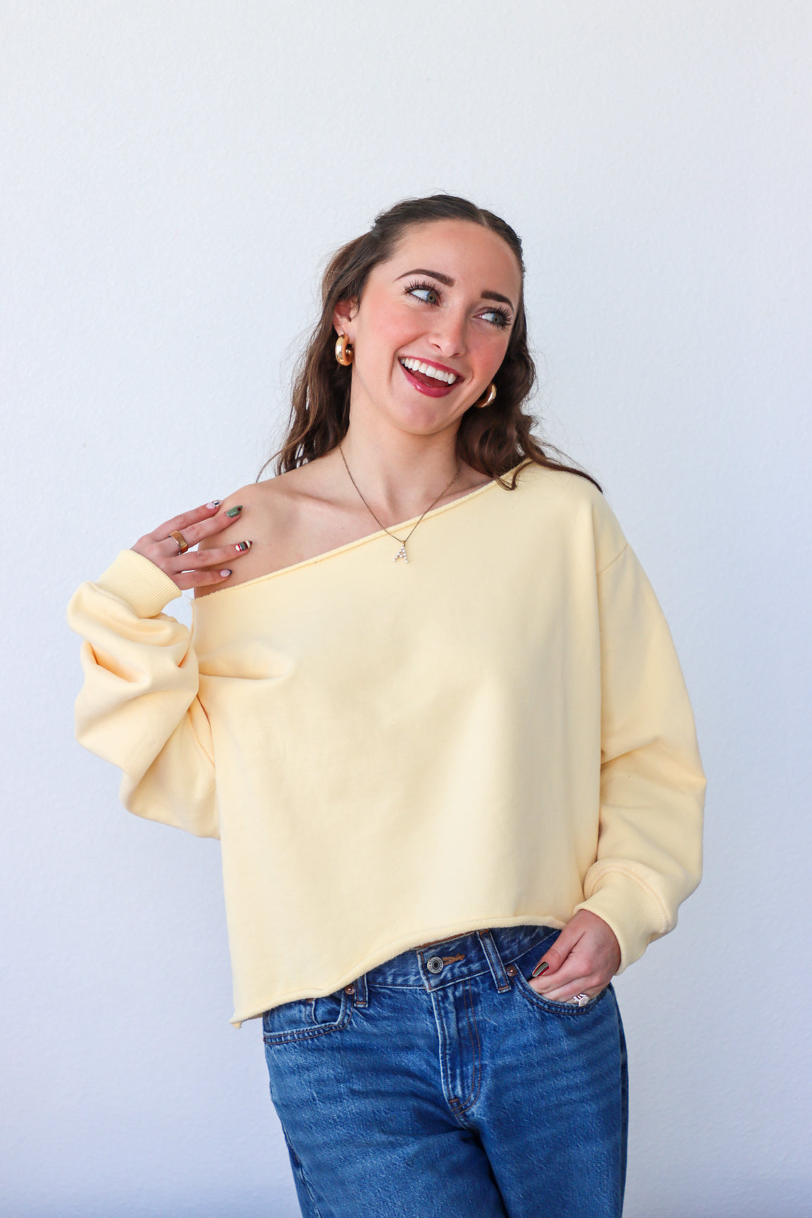 Woman wearing a yellow off-shoulder sweater and blue jeans against a white background