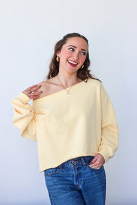 Woman wearing a yellow off-shoulder sweater and blue jeans against a white background