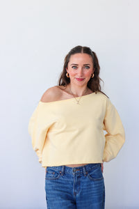 Woman wearing a yellow off-shoulder top and blue jeans against a white background