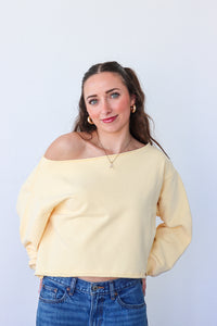 Woman wearing a yellow off-shoulder sweater and blue jeans against a white background