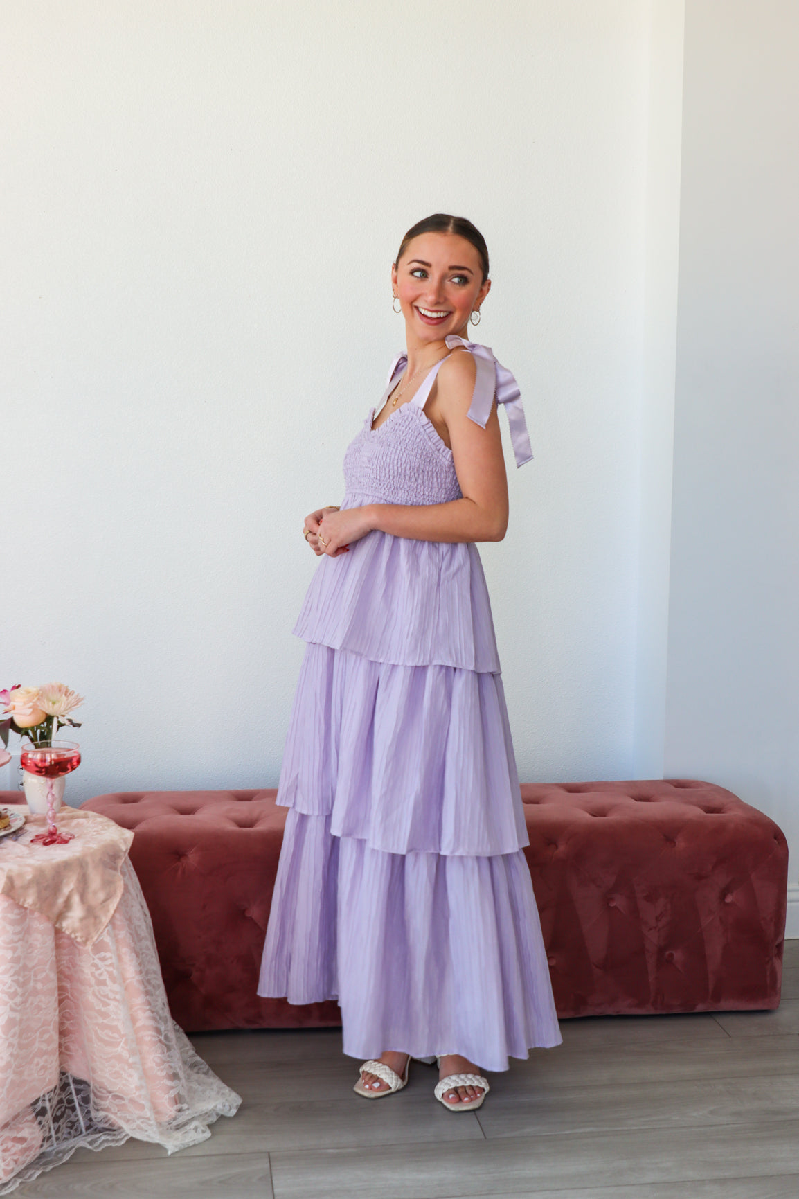 Woman in a lavender dress standing in a room with a red couch and table.