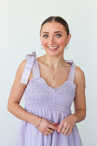 Woman wearing a light purple dress with ruffled straps against a plain background