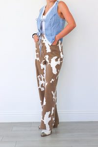 Person wearing a blue sleeveless top and brown cow print pants against a white background