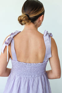 Woman wearing a light purple dress with ribbon straps on a light blue background