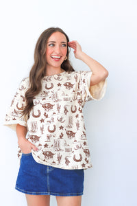Woman wearing a cream blouse with brown graphics and a blue skirt against a white background