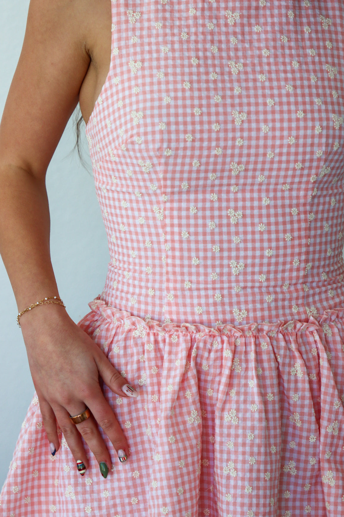 Close-up of a person wearing a pink gingham dress with a subtle floral pattern.