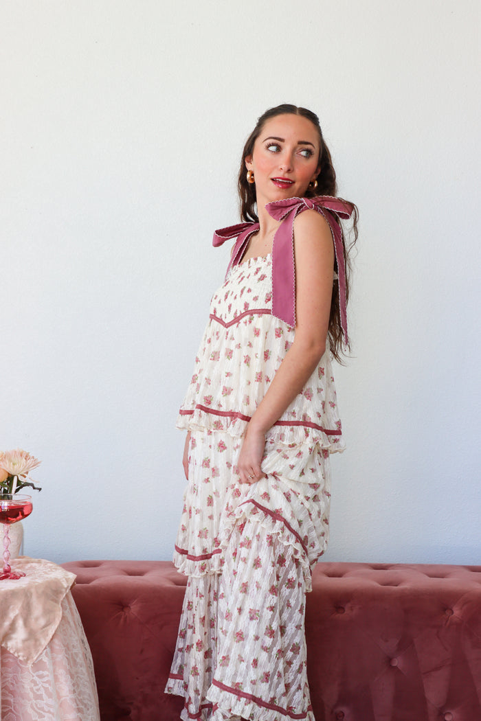 Woman wearing a floral dress with pink accents against a white wall.
