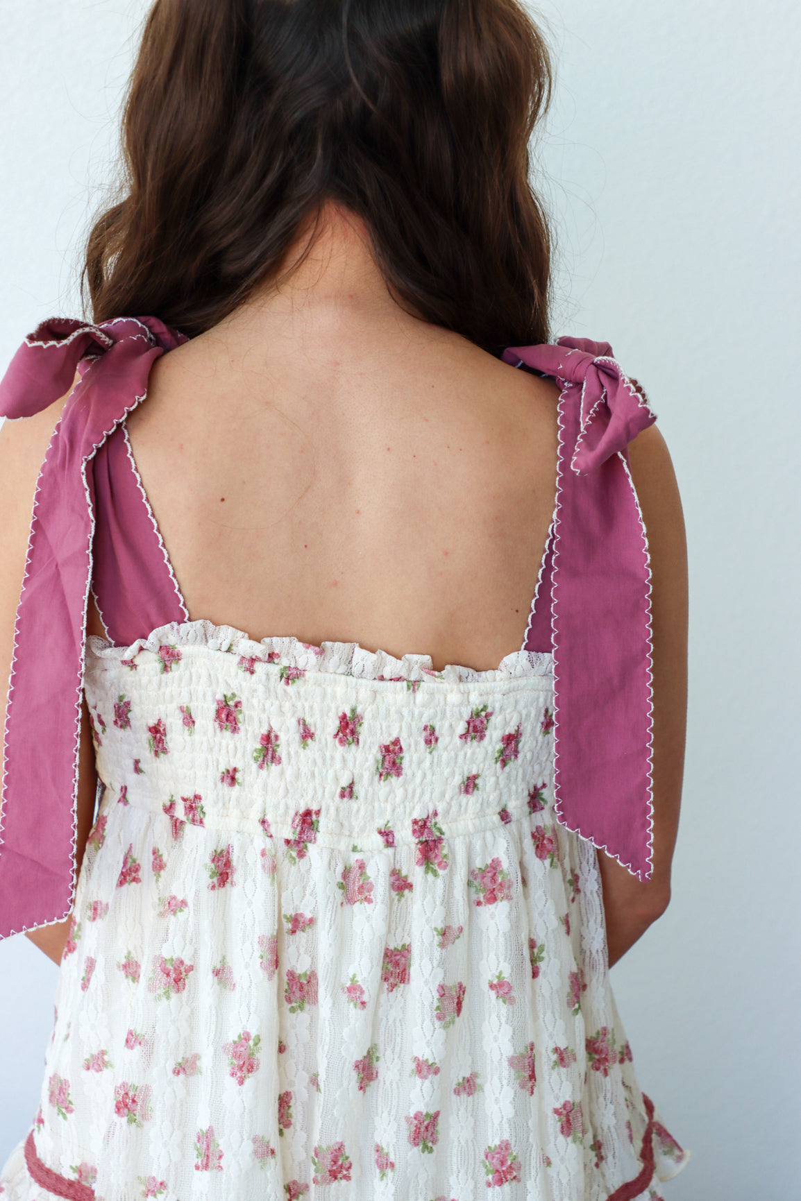 Woman wearing a white floral dress with pink ribbon straps against a light background