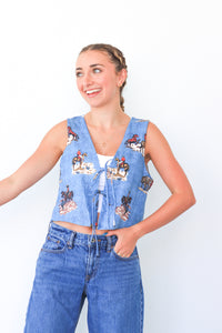 Woman wearing a denim vest with cartoon character print and blue jeans on a white background