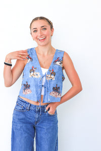 Woman wearing a blue patterned vest and jeans against a white background