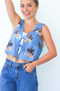 Woman wearing a blue vest with horse print and jeans on a light gray background