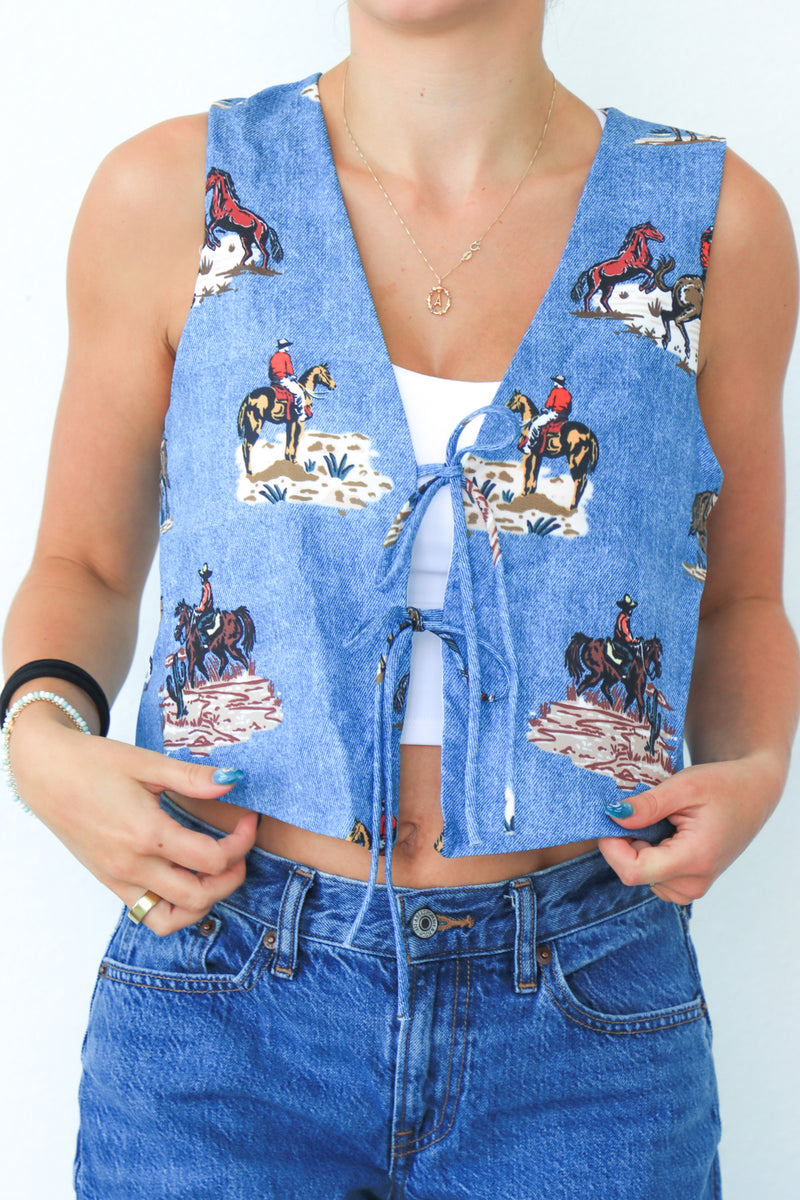 Person wearing a blue denim vest with horse print and matching jeans on a white background