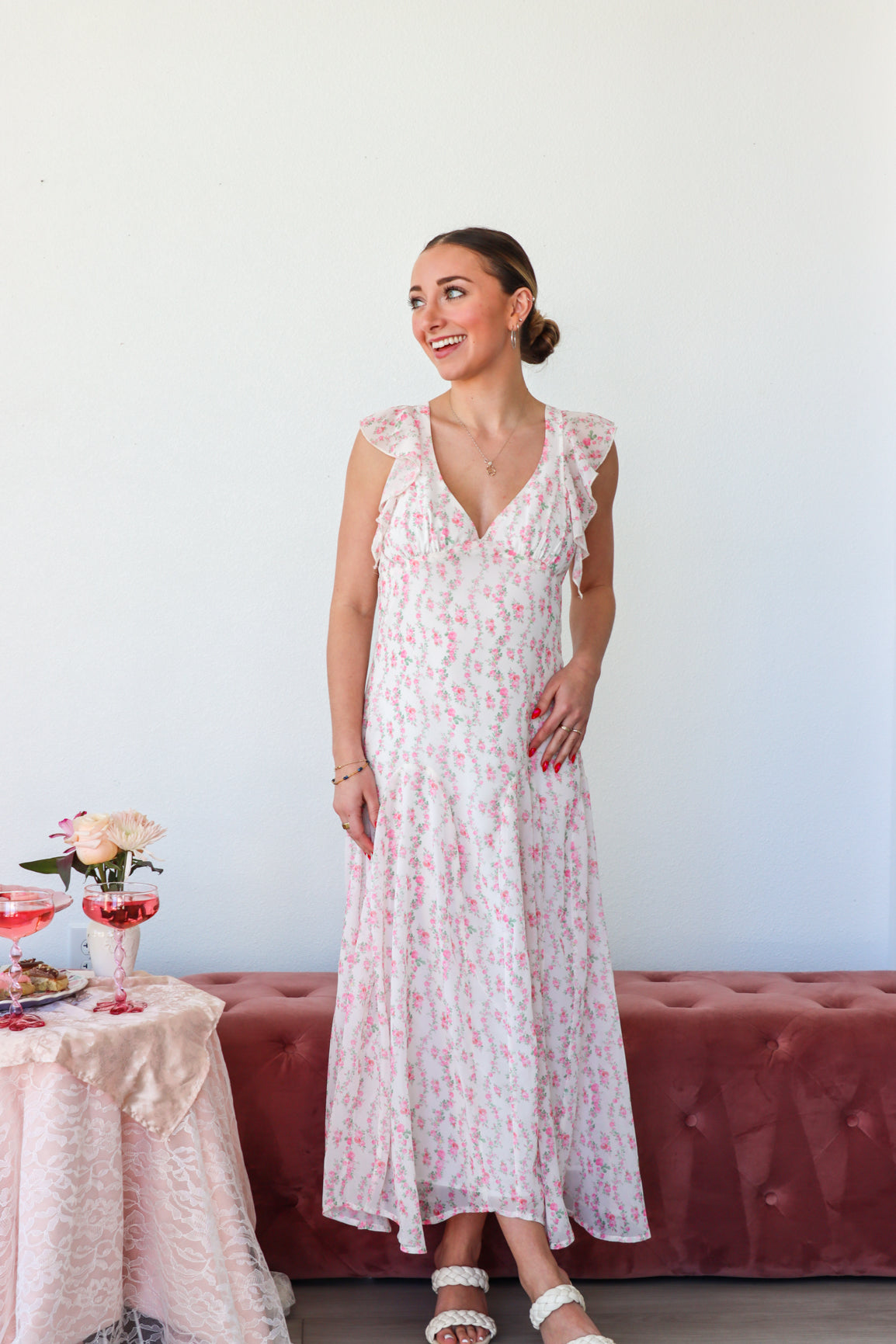 Woman in a floral dress standing in a room with a table and flowers.