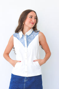 Woman wearing a white sleeveless blouse with blue lace details against a white background