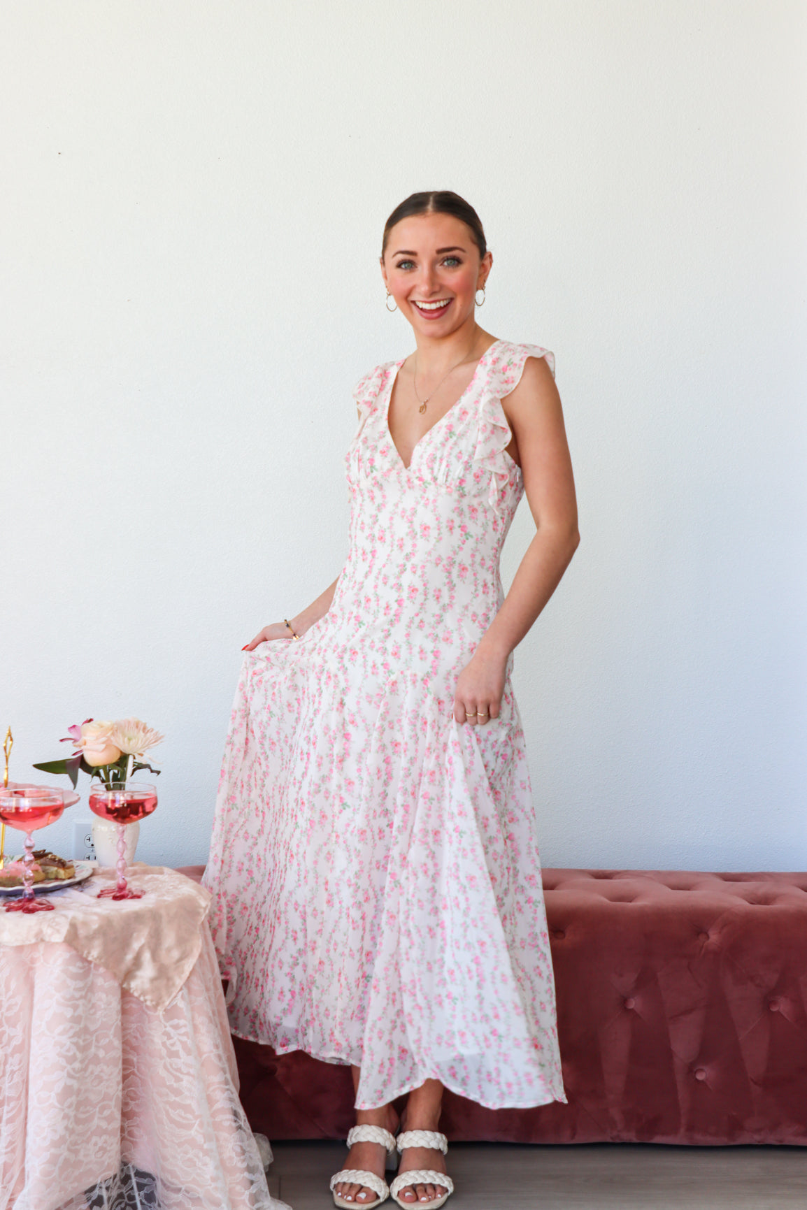 Woman in a floral dress standing in a room with a table and flowers.
