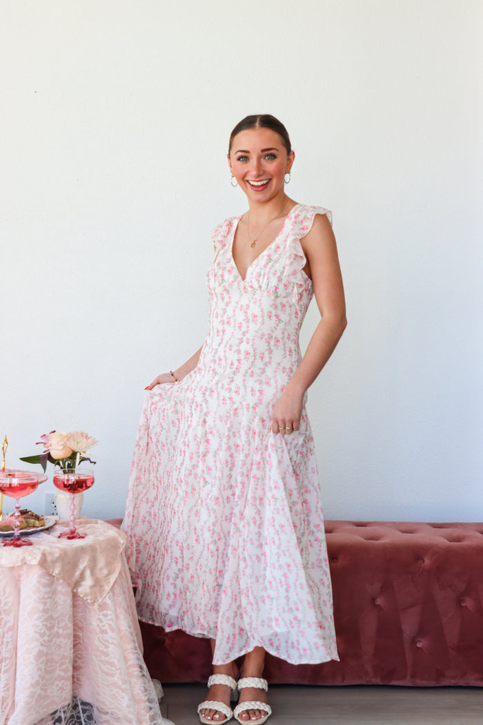 Woman in a floral dress standing in a room with a table and flowers.