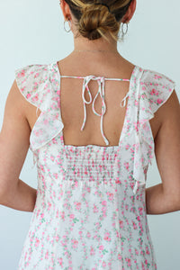 Woman wearing a floral dress with ruffled sleeves and a tied back design on a plain background