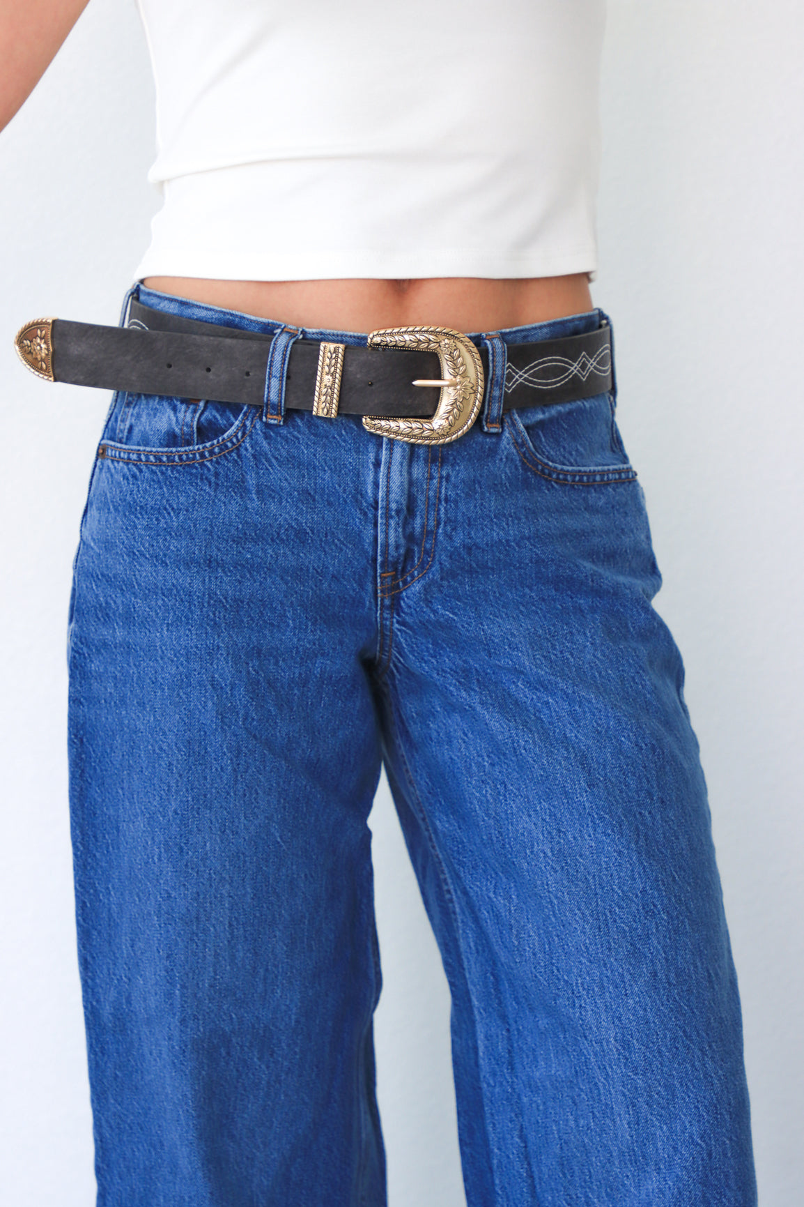 Person wearing blue jeans with a black belt and gold buckle on a white background