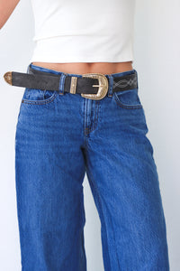 Person wearing blue jeans with a black belt and gold buckle on a white background