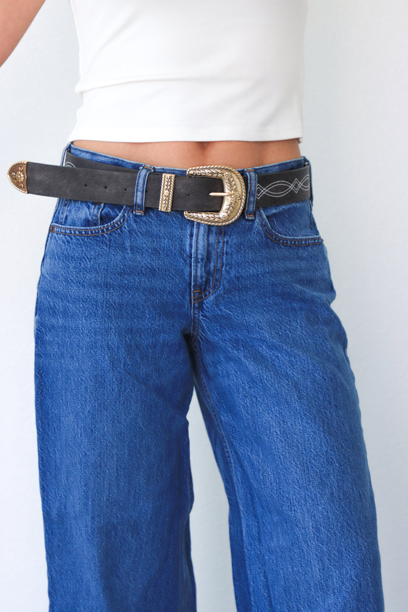 Person wearing blue jeans with a black belt and gold buckle on a white background