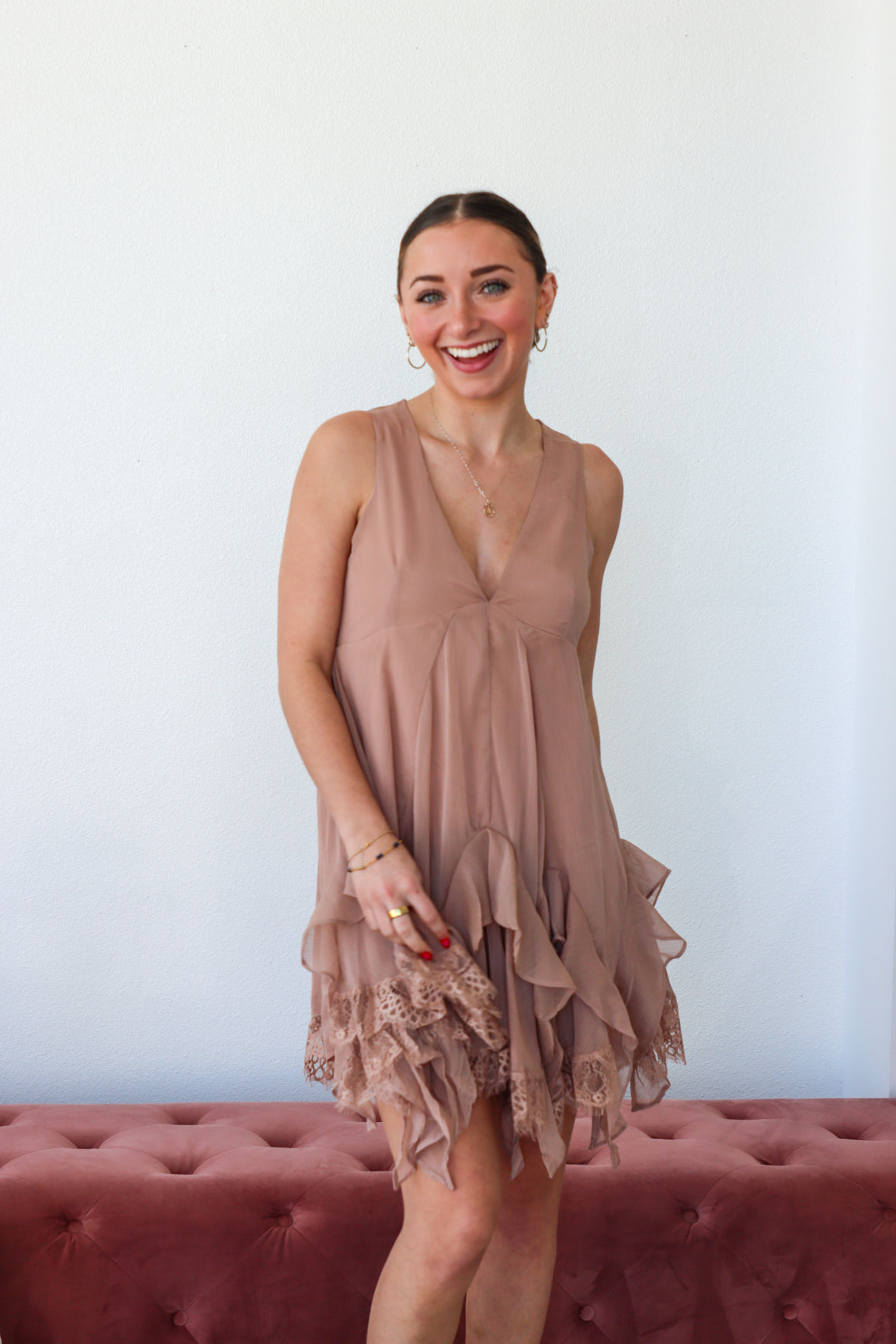 Woman wearing a beige sleeveless dress with ruffled details, standing against a white wall.
