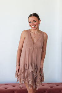 Woman wearing a beige sleeveless dress with lace details against a white background