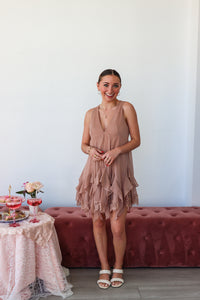 Woman in a pink dress standing next to a table with a floral arrangement and a glass of red wine.