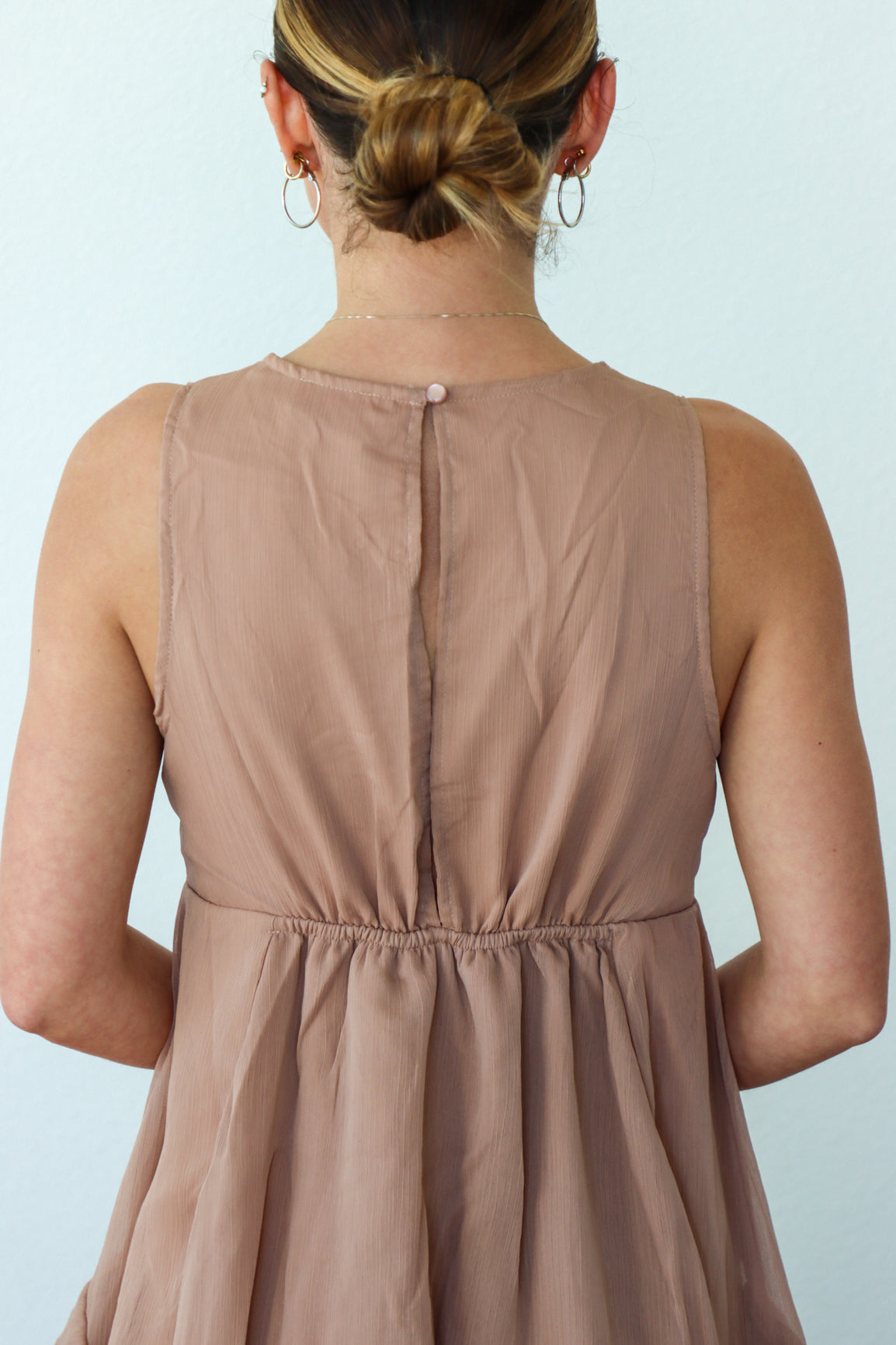 Person wearing a beige sleeveless dress against a light blue background