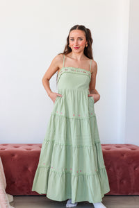 Woman wearing a green dress standing in front of a red couch with a white wall background