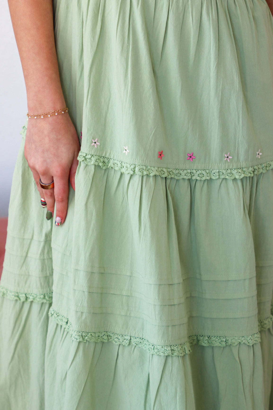 Close-up of a light green dress with lace details and floral embroidery.