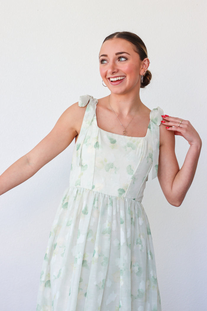 Woman wearing a light green floral dress against a white background