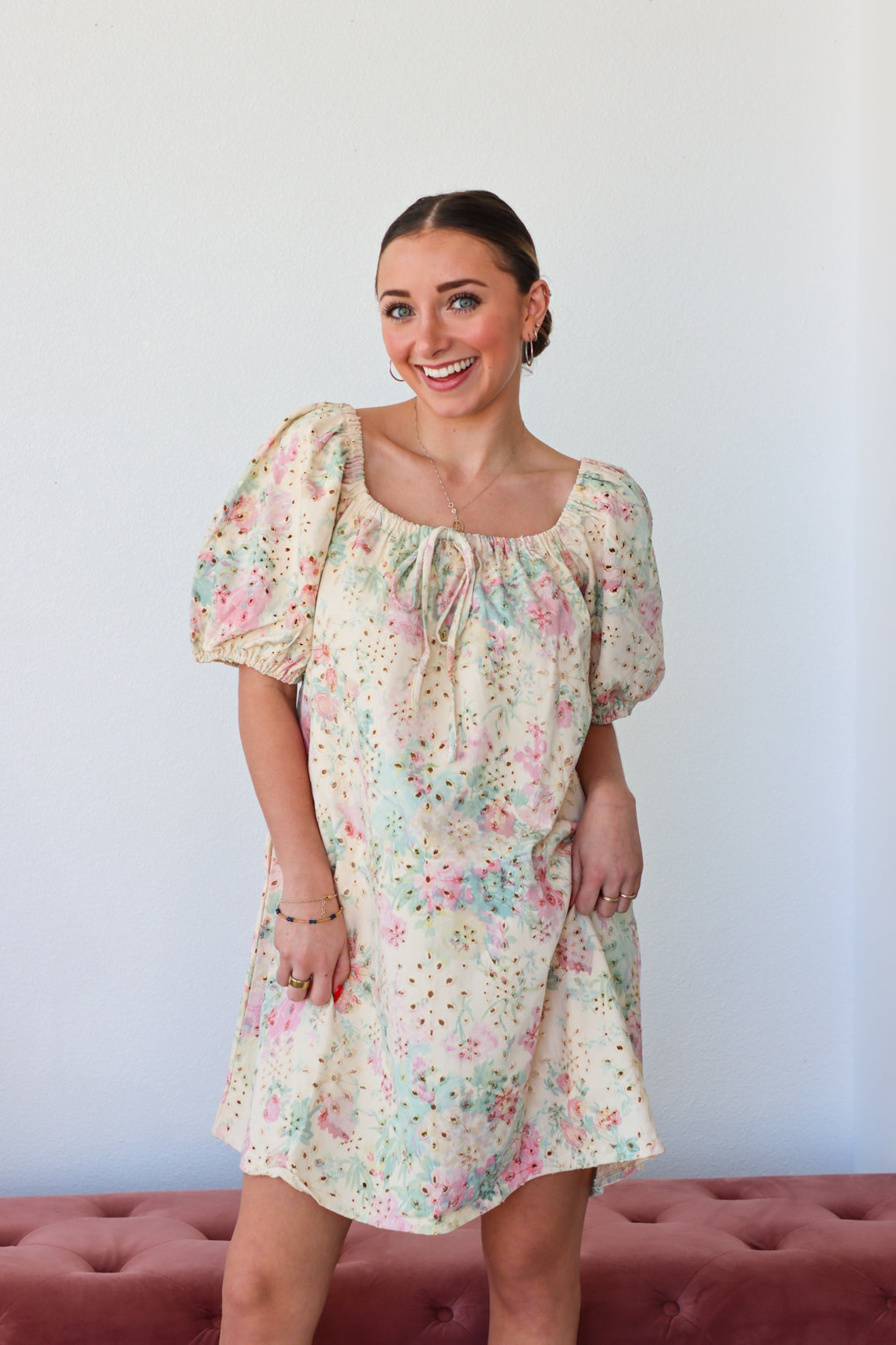 Woman wearing a floral dress standing against a plain background