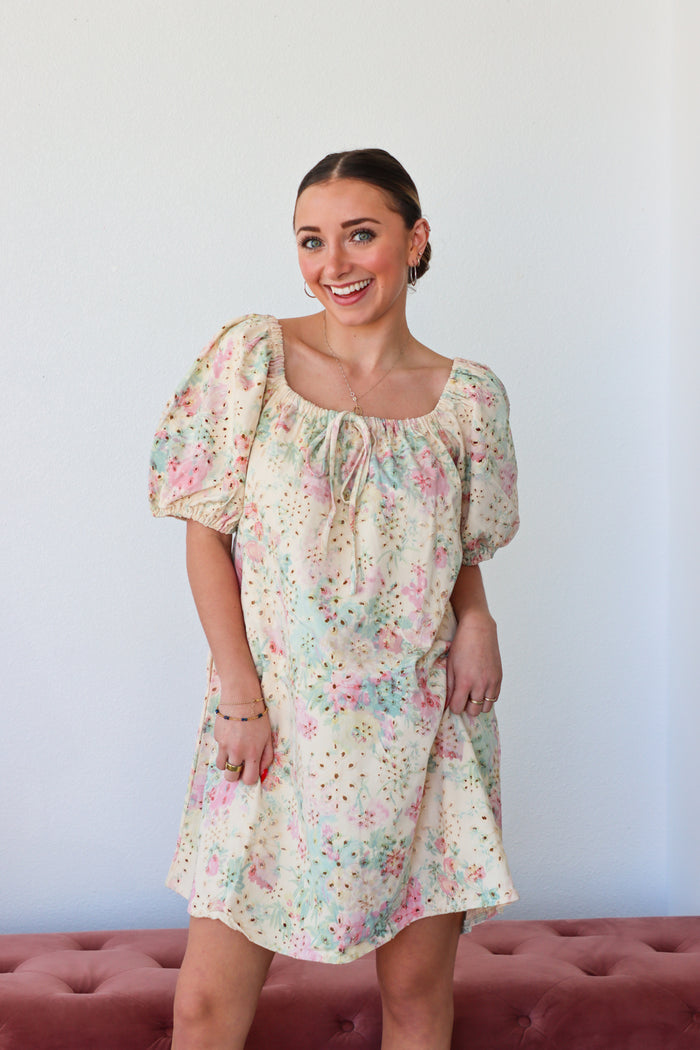 Woman wearing a floral dress standing against a plain background