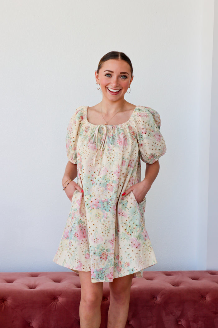 Woman wearing a floral dress standing against a white wall with a red cushioned bench.