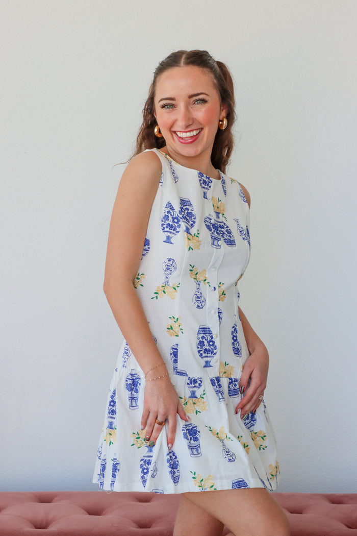 Woman wearing a white dress with blue floral patterns against a plain background