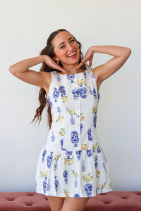 Woman wearing a white dress with blue floral patterns against a plain background