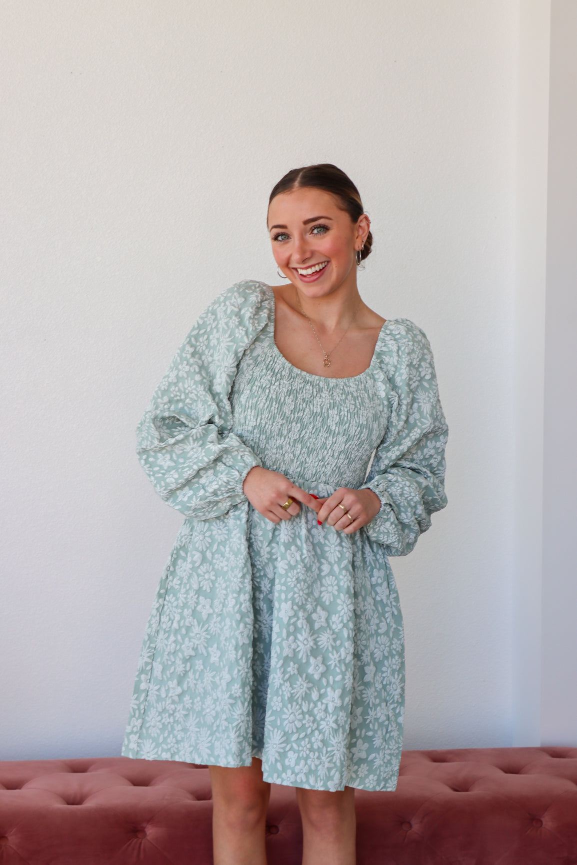Woman wearing a light blue floral dress standing against a white wall.