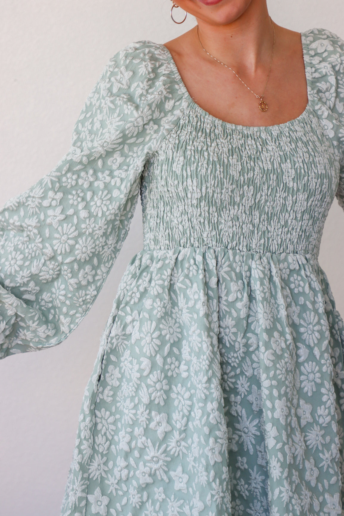 Woman wearing a light blue floral dress with long sleeves against a plain background
