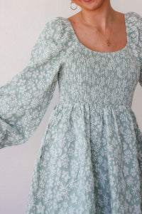 Woman wearing a light blue floral dress with long sleeves against a plain background