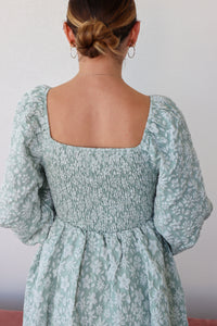 Person wearing a light blue floral dress with puffed sleeves against a plain background