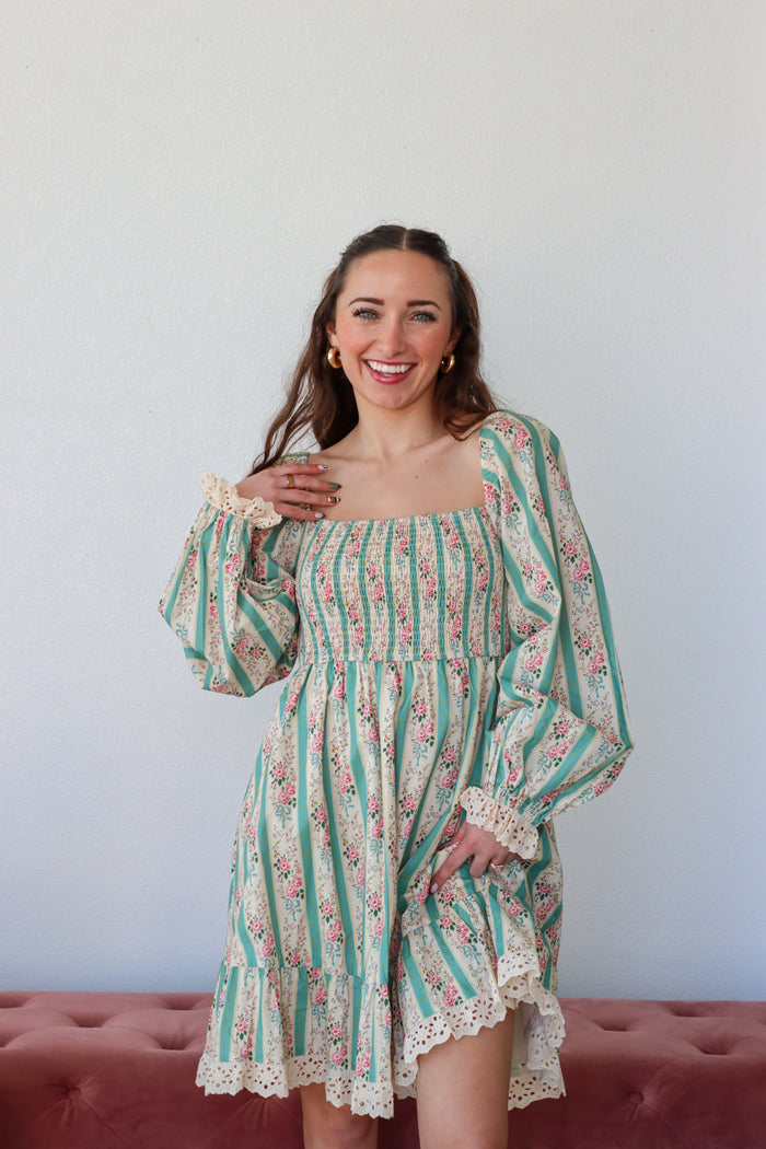Woman wearing a floral dress with long sleeves against a plain background