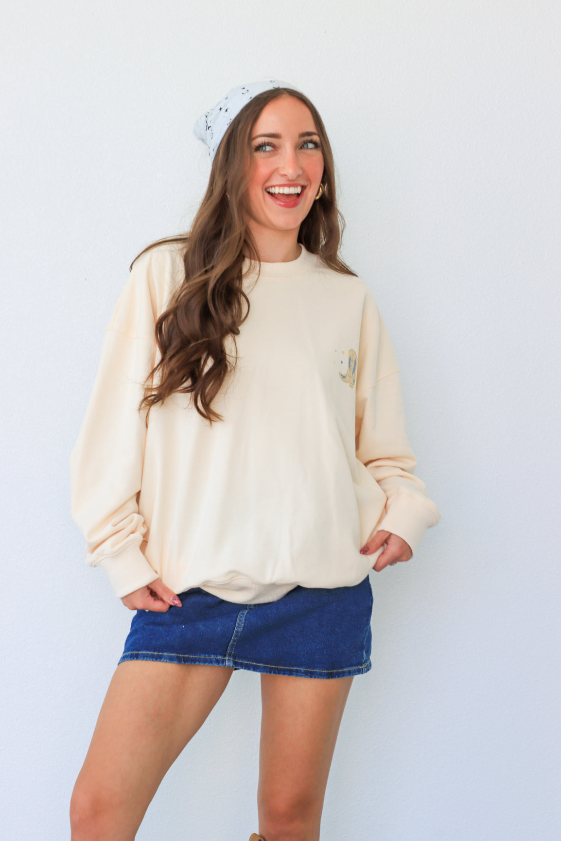 Woman wearing a cream sweater and blue denim skirt against a white background