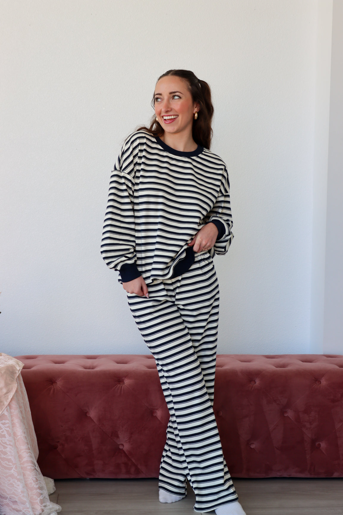 Woman wearing a black and white striped outfit standing in front of a pink sofa.