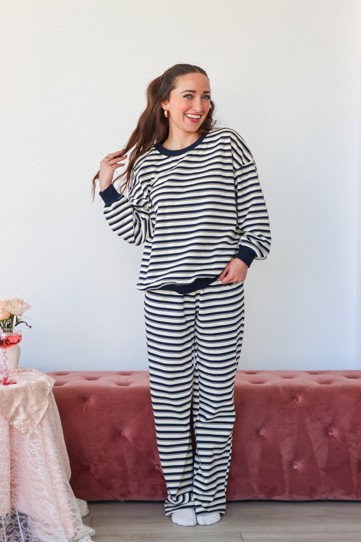 Woman wearing a black and white striped pajama set standing in a room with a pink couch and floral arrangement.