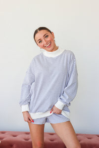 Woman wearing a blue and white striped outfit with a white turtleneck and shorts against a plain background.