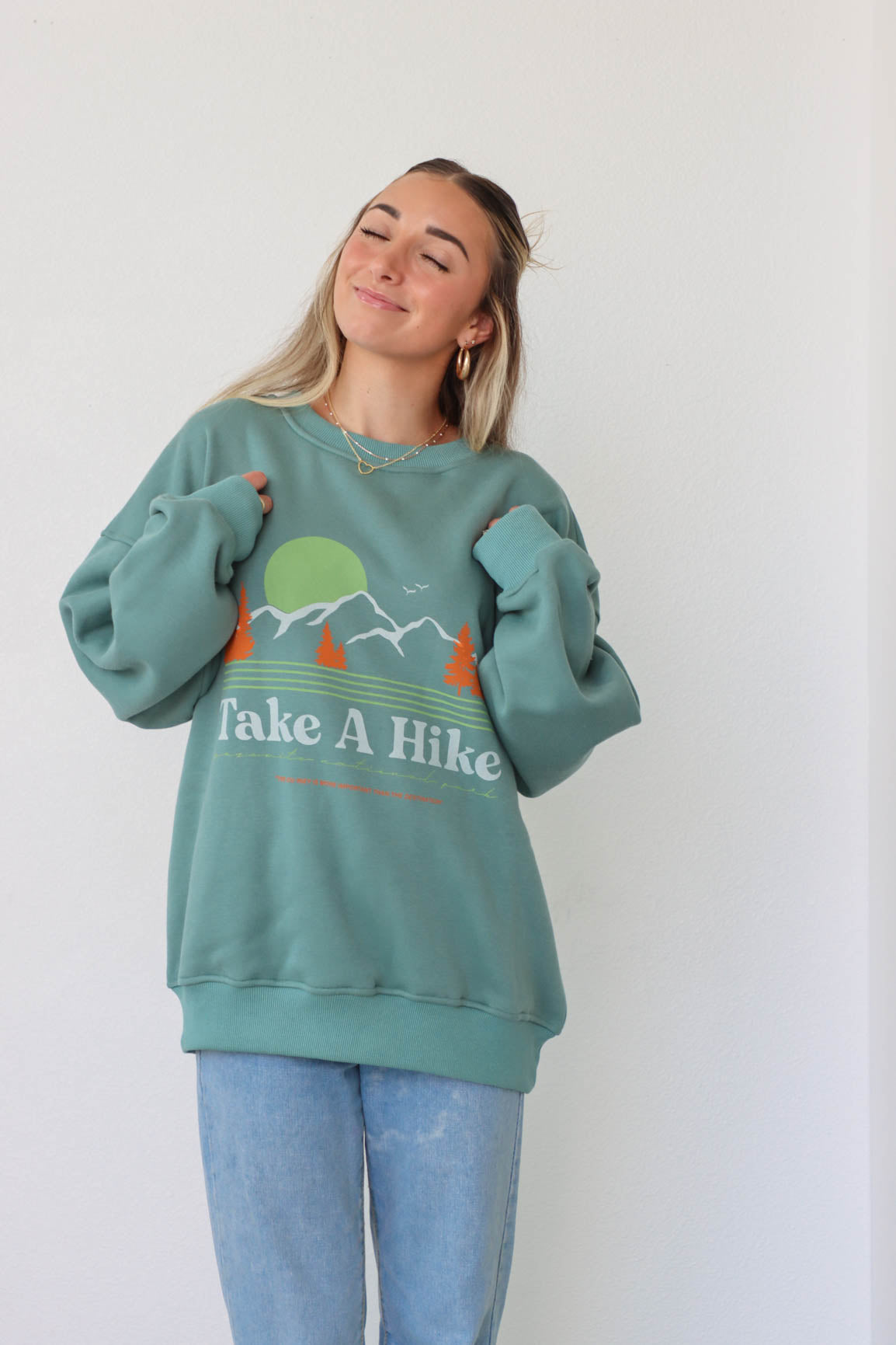 girl wearing "take a hike" green crewneck sweatshirt